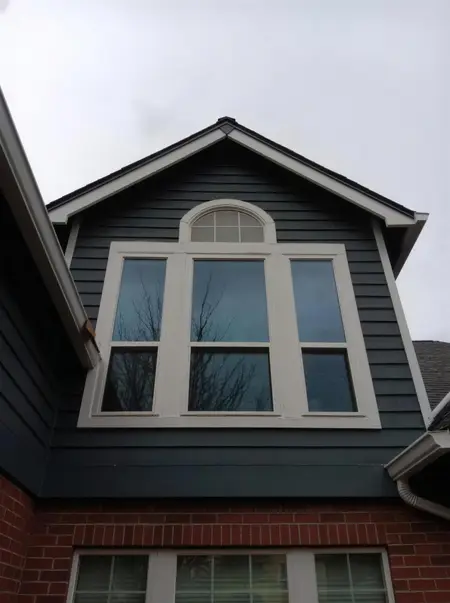 Arched transom over a three-wide window in the gable of a dark blue house above brick